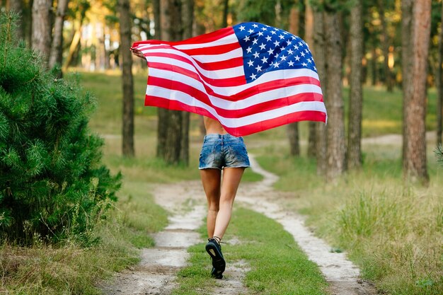 Girl in denim shorts running with American flag in hands. 