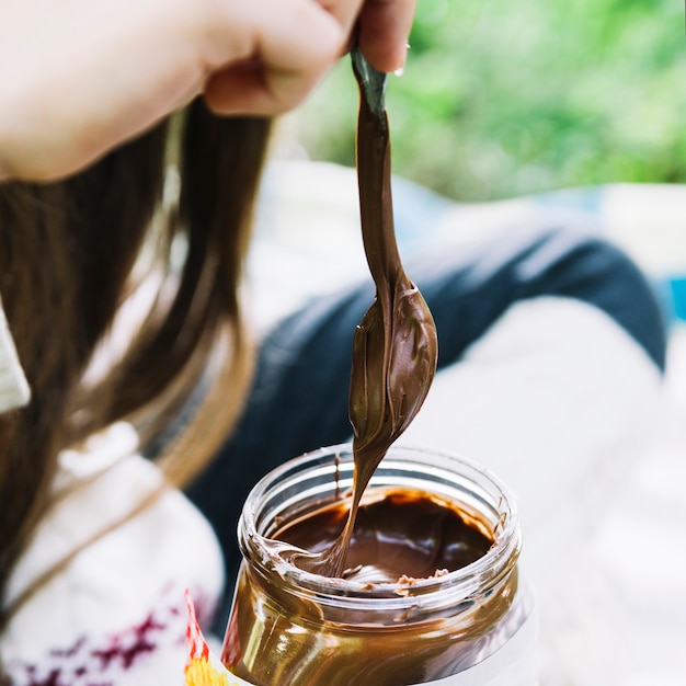 チョコレート瓶に溶かしてスプーンを浸す少女