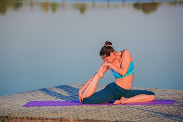 Foto gratuita ragazza che fa esercizi di yoga sulla riva del fiume al tramonto