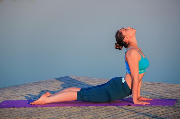 Foto gratuita ragazza che fa esercizi di yoga sulla riva del fiume al tramonto