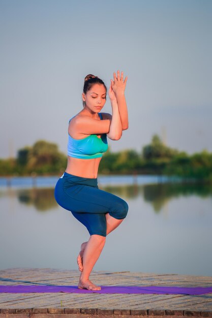 girl doing yoga exercises on the river bank at sunset