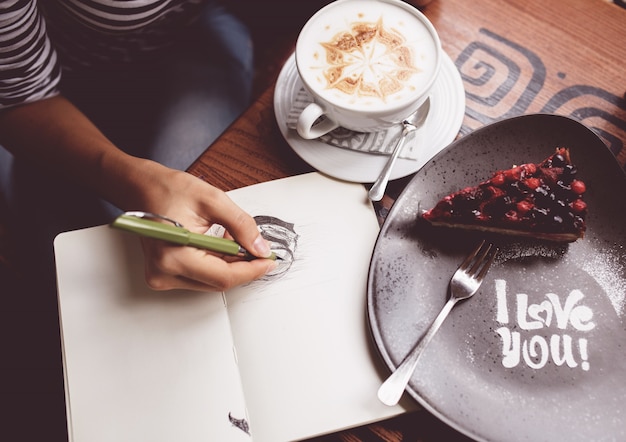 Girl drawing a cup of coffee in the notebook