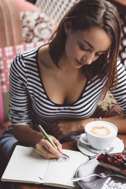 Free photo girl drawing a cup of coffee in the notebook