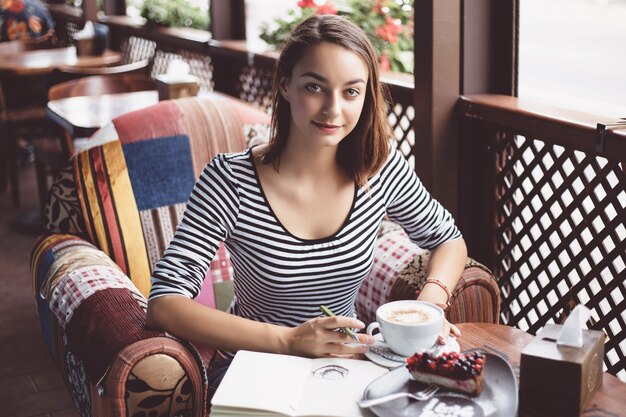 Girl drawing a cup of coffee in the notebook