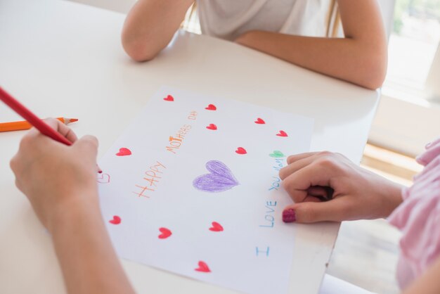 Girl drawing hearts on paper with Happy Mothers Day inscription 