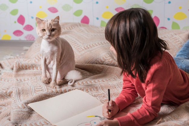 Free photo girl drawing on paper looking at cat