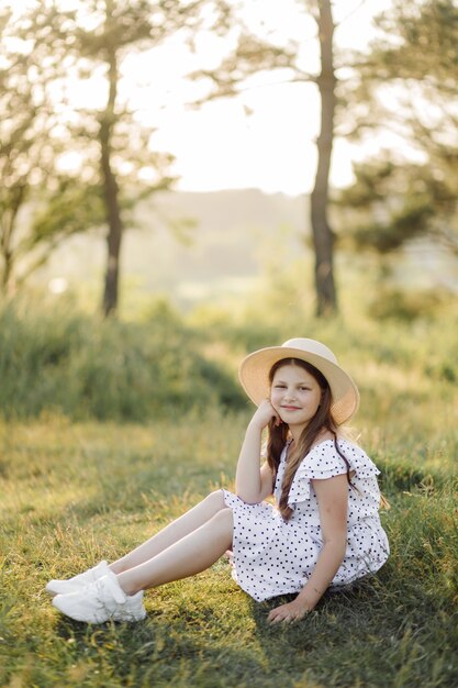 A girl in a dress and a hat stands in the field