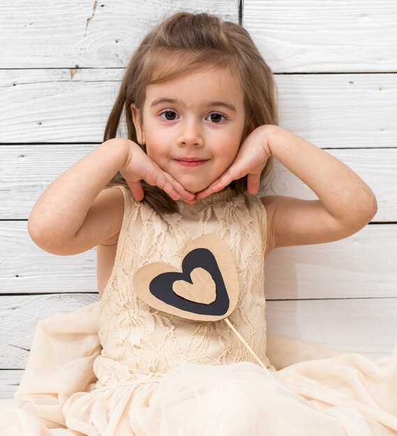 девушка в платье сидит на белом деревянном фоне с сердцем в руках