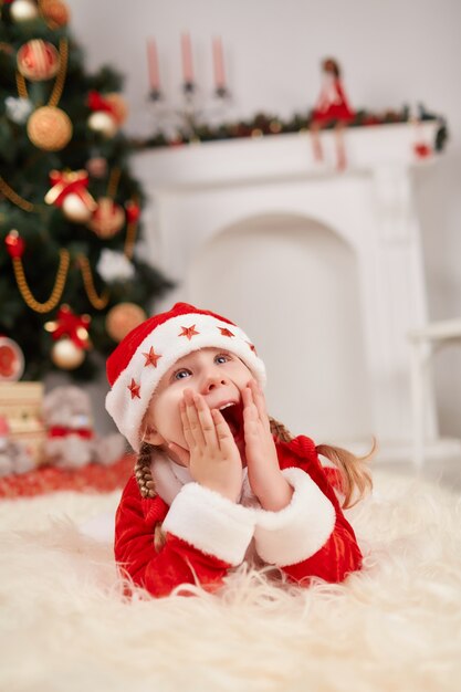 Girl dressed in santa claus lying on the floor with hands on face