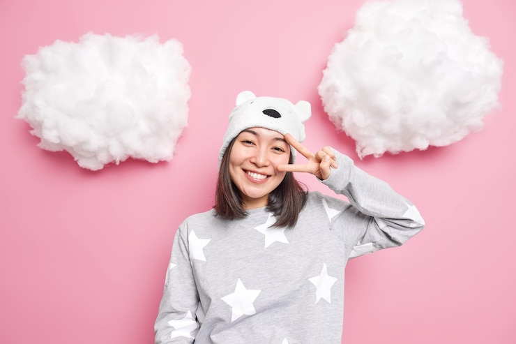 Free Photo girl dressed in slumber suit shows peace gesture near life enjoys life smiles carefree poses cheerful tilts head isolated on pink