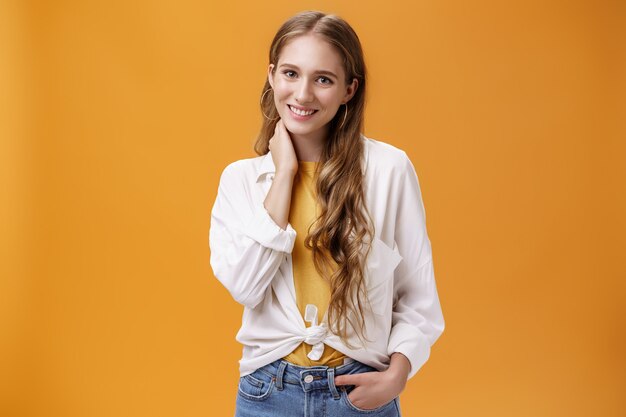 Girl dressing up for success. Charming feminine and stylish young female with wavy natural hairstyle touching neck timid and shy smiling cheerfully at camera wearing large earrings and blouse.