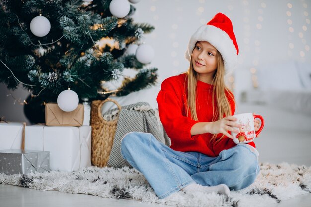 Girl drinking cocoa by christmas tree