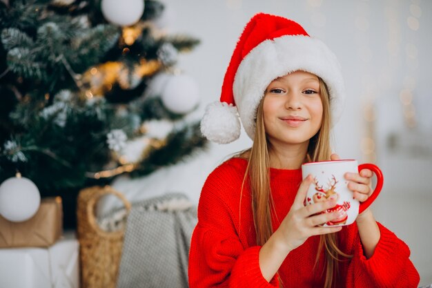 Girl drinking cocoa by christmas tree