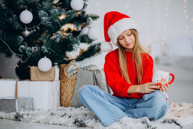 Girl drinking cocoa by christmas tree