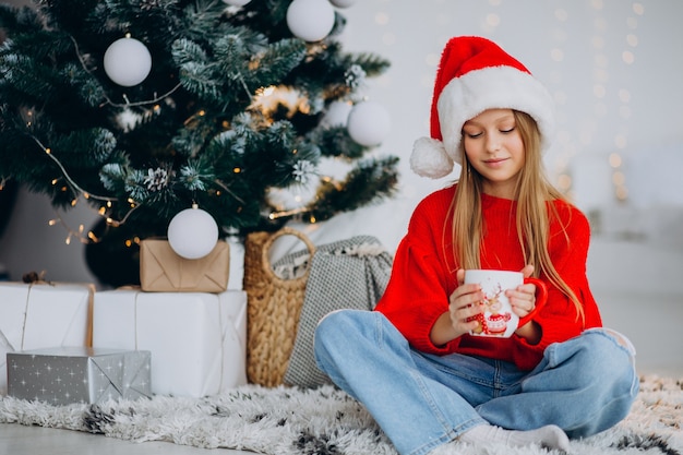 Girl drinking cocoa by christmas tree