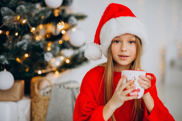 Girl drinking cocoa by christmas tree