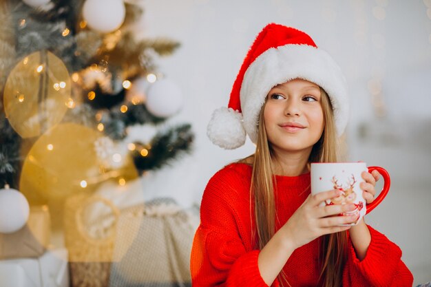 Girl drinking cocoa by christmas tree