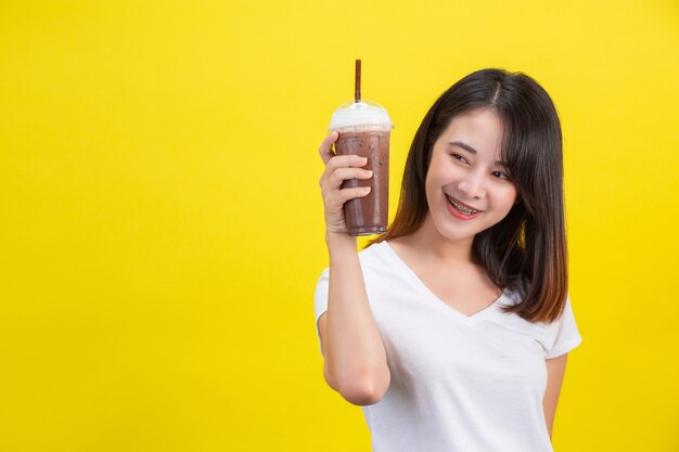 女の子は黄色の透明なプラスチックガラスからココアの冷たい水を飲みます。