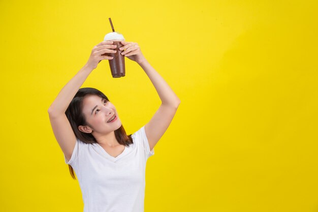 女の子は黄色の透明なプラスチックガラスからココアの冷たい水を飲みます。