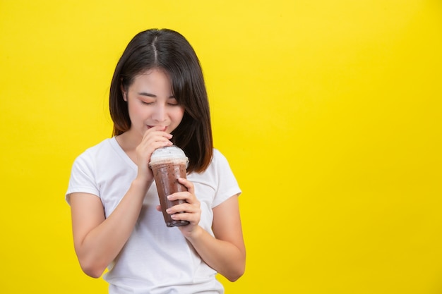 女の子は黄色の透明なプラスチックガラスからココアの冷たい水を飲みます。