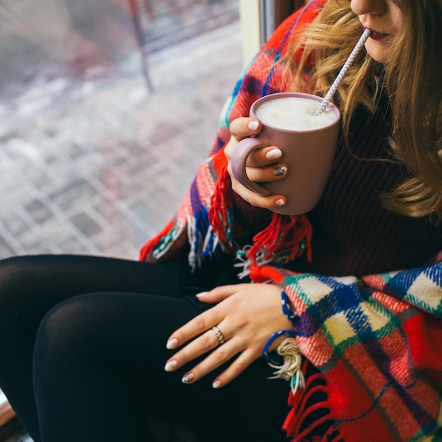 Бесплатное фото Девушка выпивает горячий шоколад из чашки сидит окутанный пледом