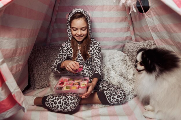 Girl eating candies in an indoors tent and dog