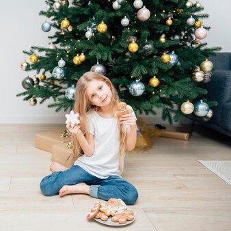 Девушка ест рождественские пряники возле елки в гостиной