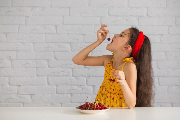 レンガの壁の前で赤い新鮮な喜びを食べる少女
