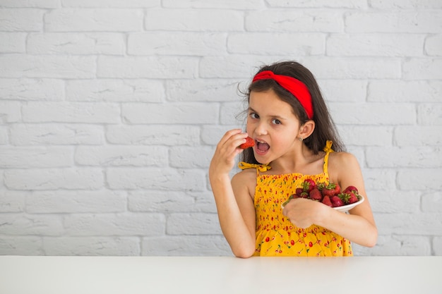 Girl eating red strawberry from plate