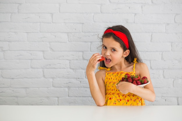 プレートから赤いイチゴを食べる少女