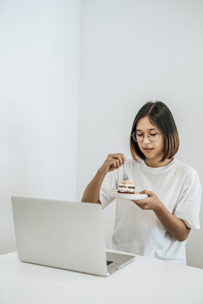 The girl eats cake and has a laptop on the table.