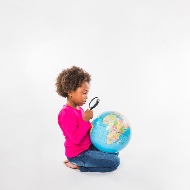 Girl exploring globe with loupe in studio