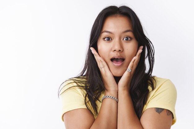 Girl expressing surprise and amazement as hearing incredible good news reacting on awesome gossip enertained and amused gasping dropping jaw from amazement and holding palms on face