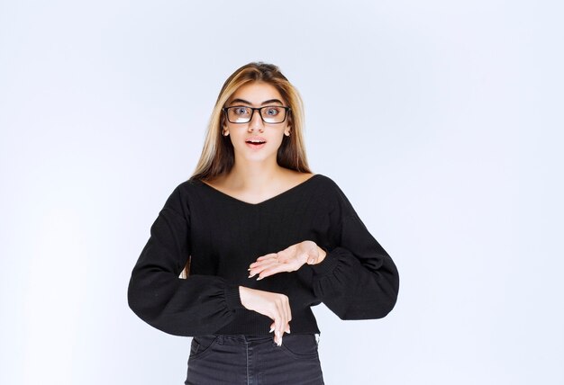 Girl in eyeglasses pointing at her watch.