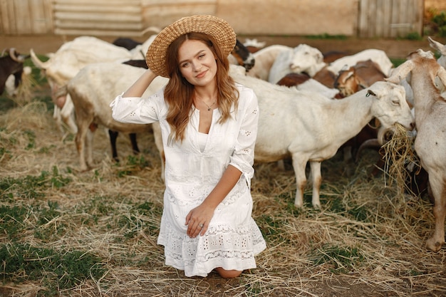 白ヤギの少女農夫。女性と小さなヤギの緑の草。エコファーム。農場と農業の概念。村の動物。女の子はかわいいヤギを再生します。 F