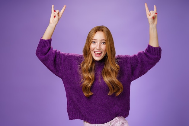 Girl feeling excited finally receiving tickets for favorite band show, raising hands with rock-n-roll gesture yelling yeah and smiling broadly, happy and thrilled against purple background. Copy space