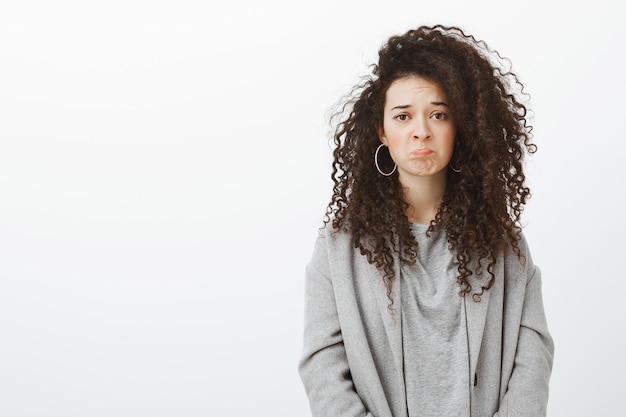 Free photo girl feels regret missing interesting movie in cinema. sulking sad attractive curly-haired female in stylish clothes and earrings, grimacing, feeling upset and disappointed