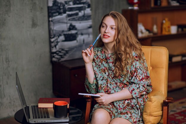 Girl in floral dress sitting and taking notes at her notebook.