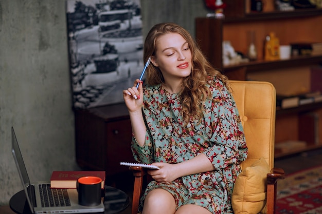 Girl in floral dress sitting and taking notes at her notebook.