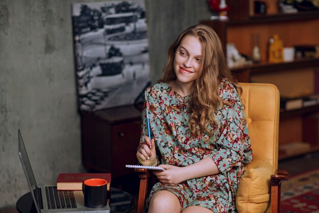 Girl in floral dress sitting and taking notes at her notebook.