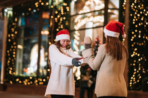 The girl gives a gift to her female friend on the street. Portrait of happy cute young friends