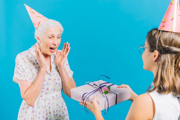 Девушка дает подарок на день рождения удивленной бабушке на синем фоне