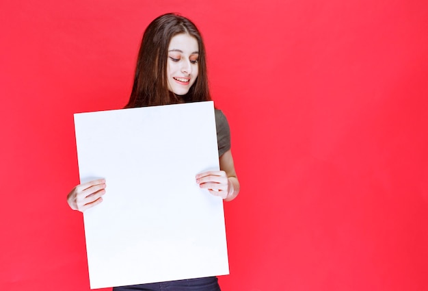 Girl in green shirt holding a big blank square info desk. 