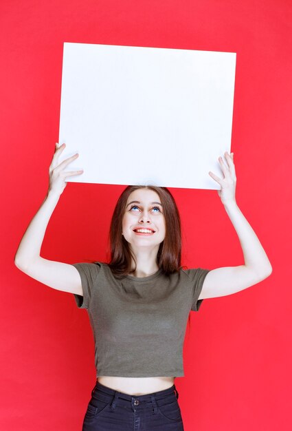 Girl in green shirt holding a big blank square info desk. 