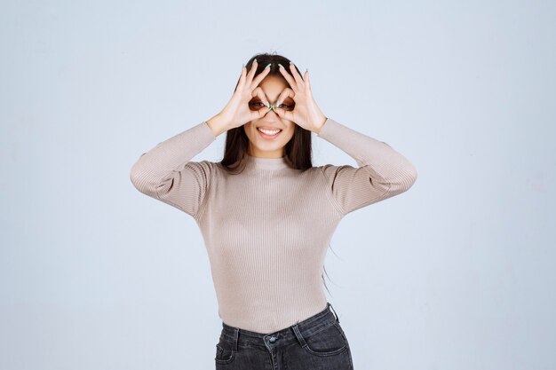 Girl in grey shirt looking through fingers. 