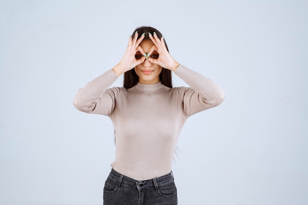 Girl in grey shirt looking through fingers. 