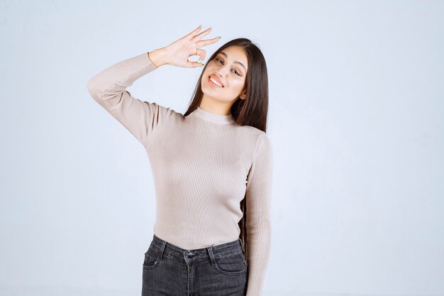 Ragazza in camicia grigia che punta alla bocca.