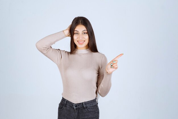 Ragazza in camicia grigia che punta a destra.