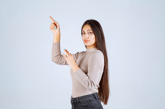 Girl in grey shirt pointing to something up. 
