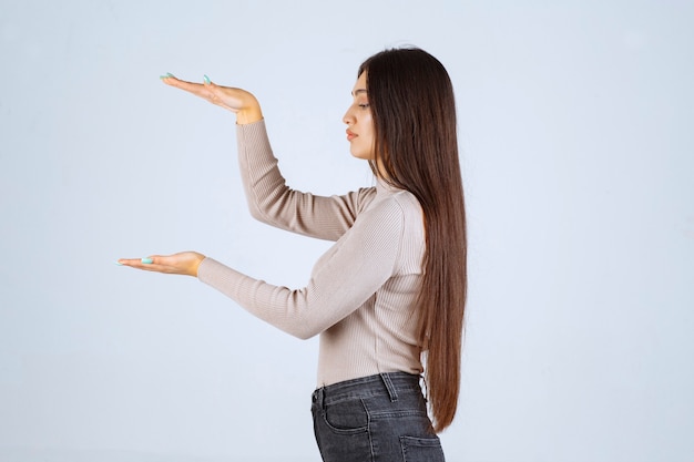 Foto gratuita ragazza in camicia grigia che mostra le misure stimate di un oggetto.